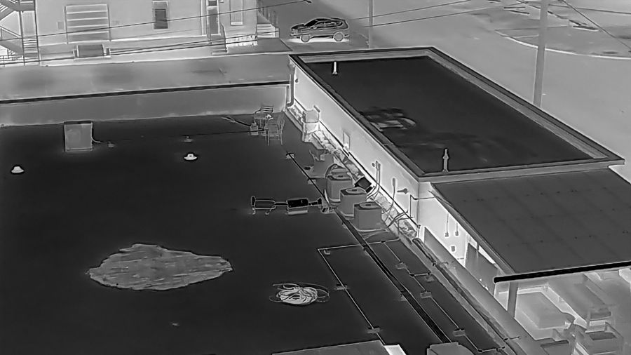 Aerial radiometric thermal image of a flat commercial roof captured by VSD Pros, a bright anomaly marking likely trapped moisture under the membrane